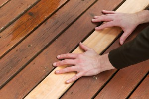 Horizontal photo of male hands putting in a single new cedar wooden board next to fading wood on outdoor deck